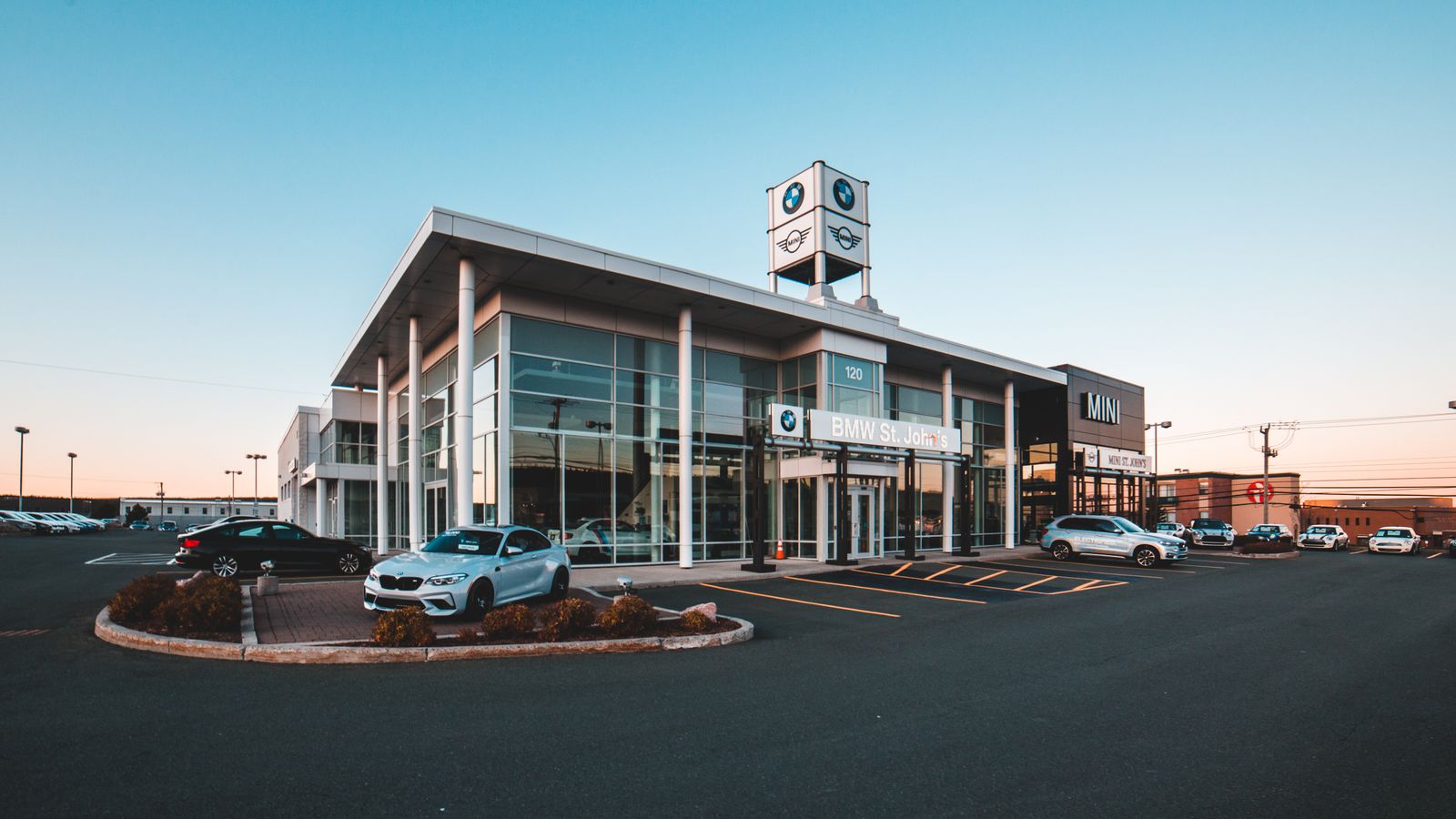 Cars displayed outside a modern BMW and MINI dealership at dusk