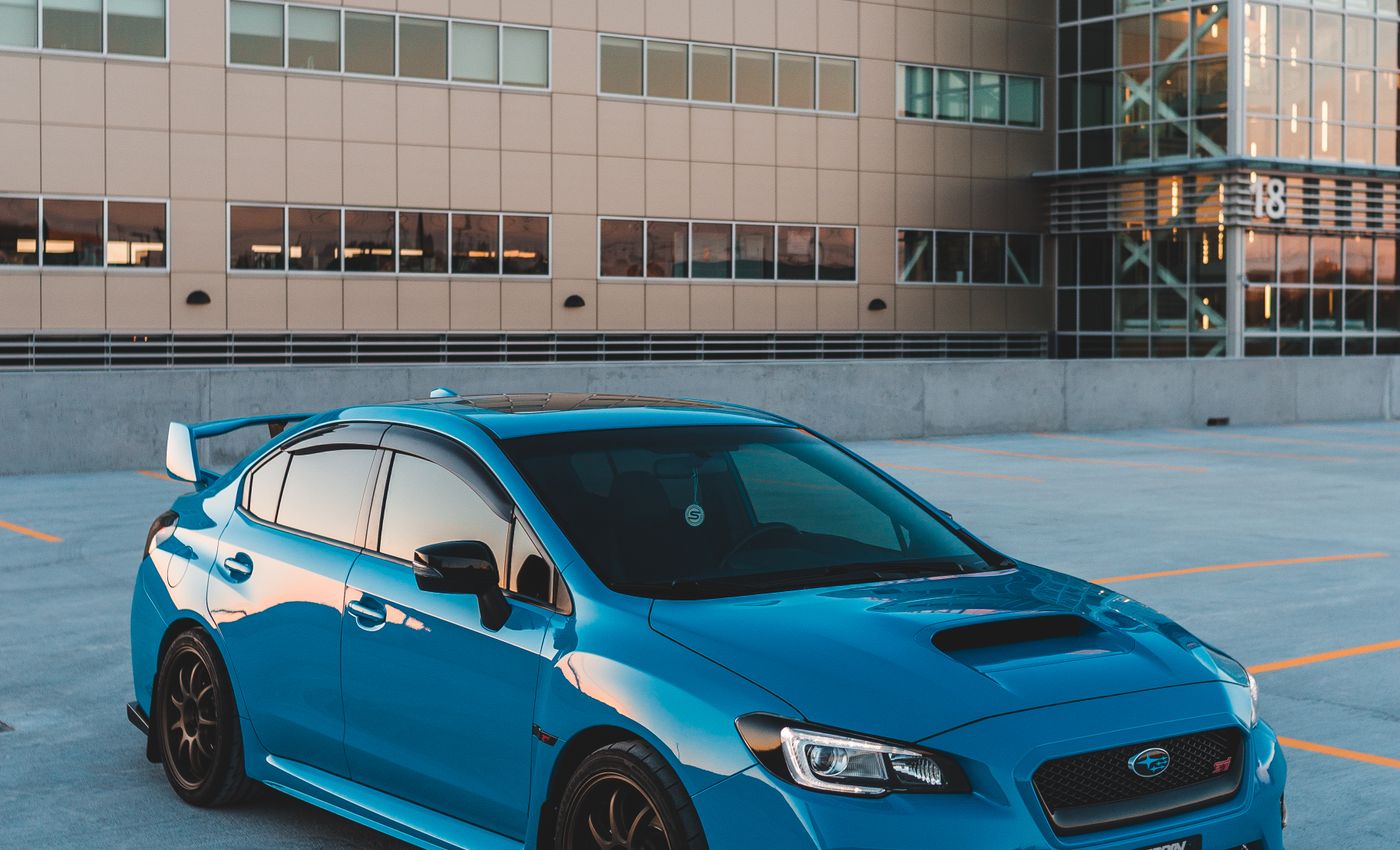 A blue Subaru parked outside a modern building in evening light