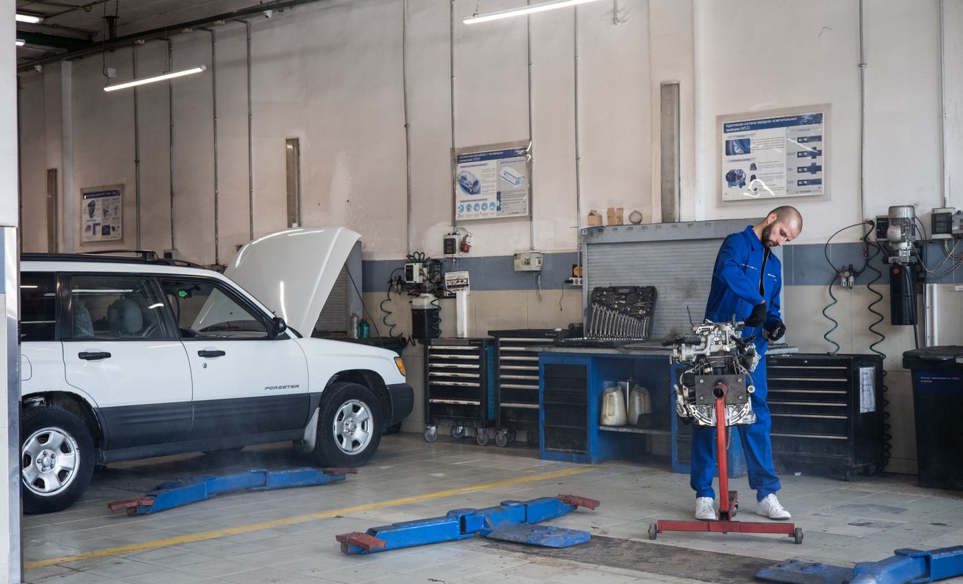 Mechanic in blue overalls working on an engine beside a car in a workshop