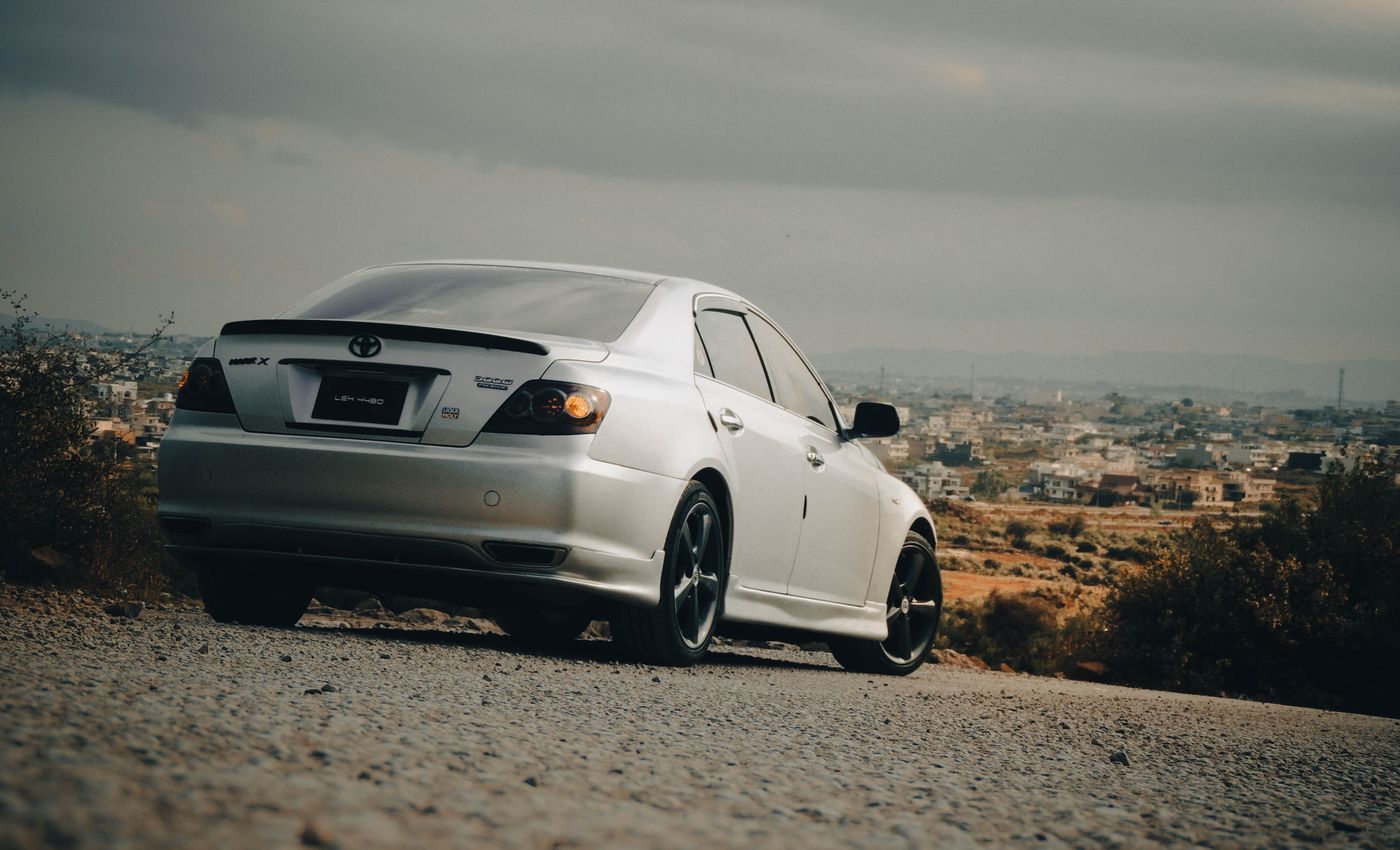 A silver Toyota saloon parked on a hillside overlooking a city