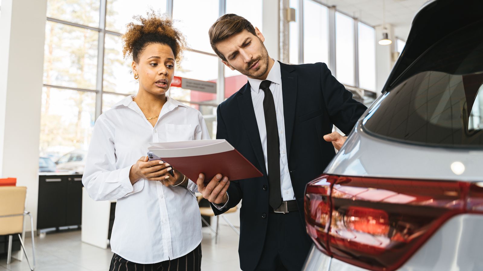 Two people discussing vehicle paperwork beside a car in a showroom